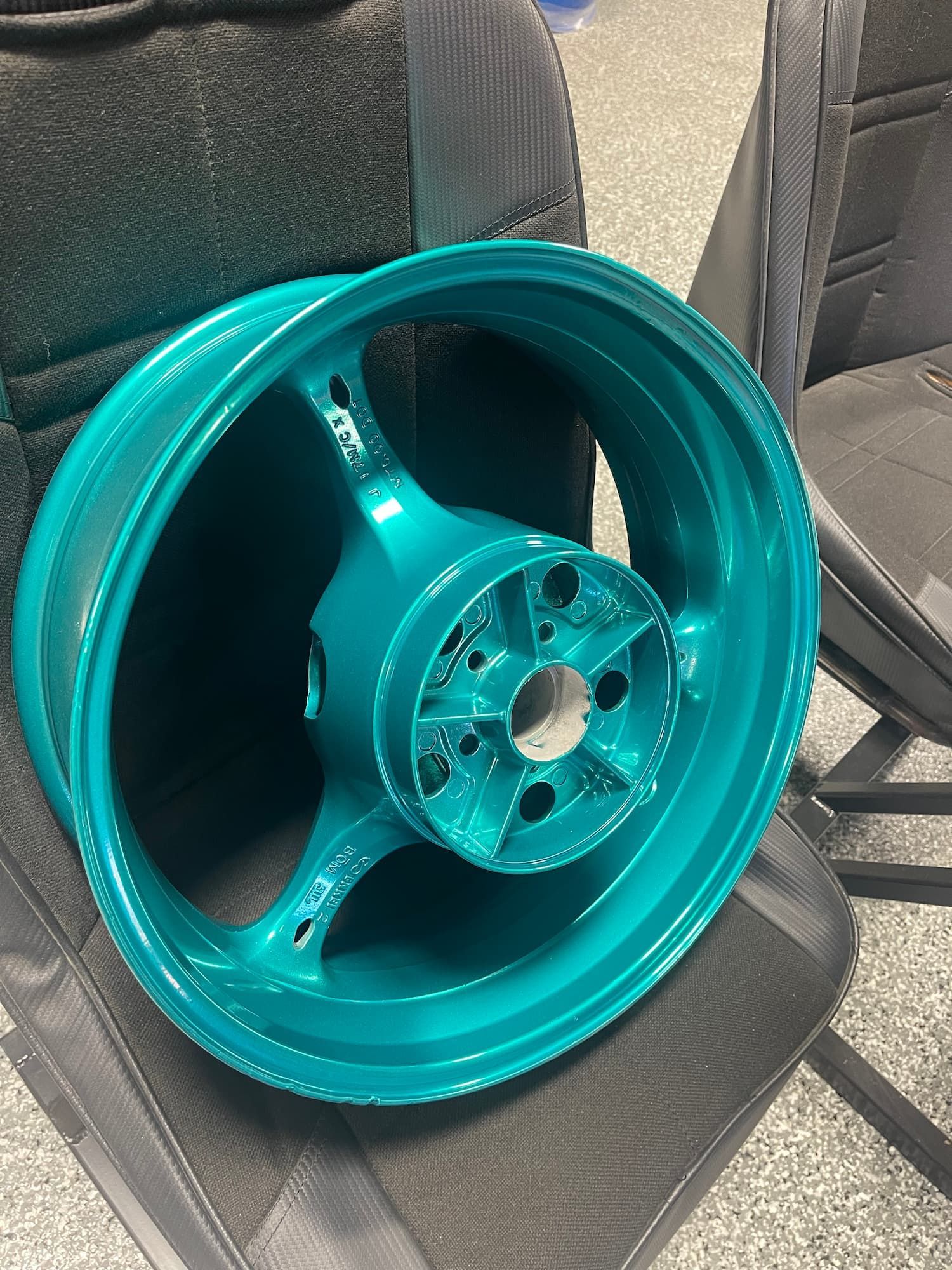 Turquoise car wheel rim resting on a black chair, shown indoors.