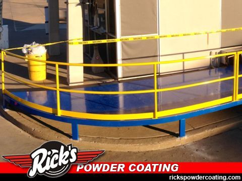 Yellow-and-blue industrial platform with safety railings beside large tanks, branded Rick’s Powder Coating.