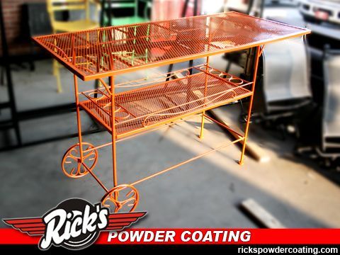 Orange powder-coated metal cart with two shelves and wheels, displayed outdoors with Rick’s Powder Coating branding