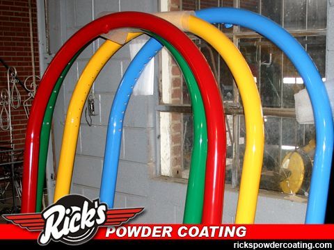 Colorful powder-coated metal tubes leaning in a workshop, with Rick’s Powder Coating logo visible.