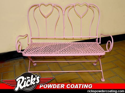 Pink wrought-iron bench with heart-shaped backs and floral mesh seat on a tiled floor