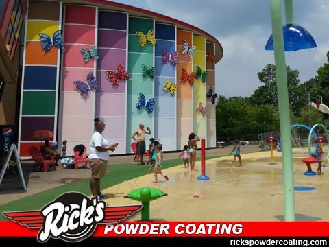 Colorful splash pad with children playing beside a butterfly-painted building and water jets