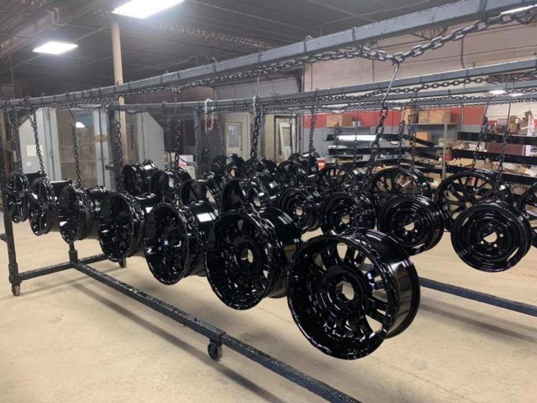 Rows of glossy black wheel assemblies hanging in an industrial workshop, drying on metal racks
