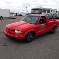 Red pickup truck parked on asphalt in front of a white RV and trailer.