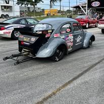 Black vintage drag car on a racetrack, viewed from the rear with sponsor decals and parachute chute deployed.