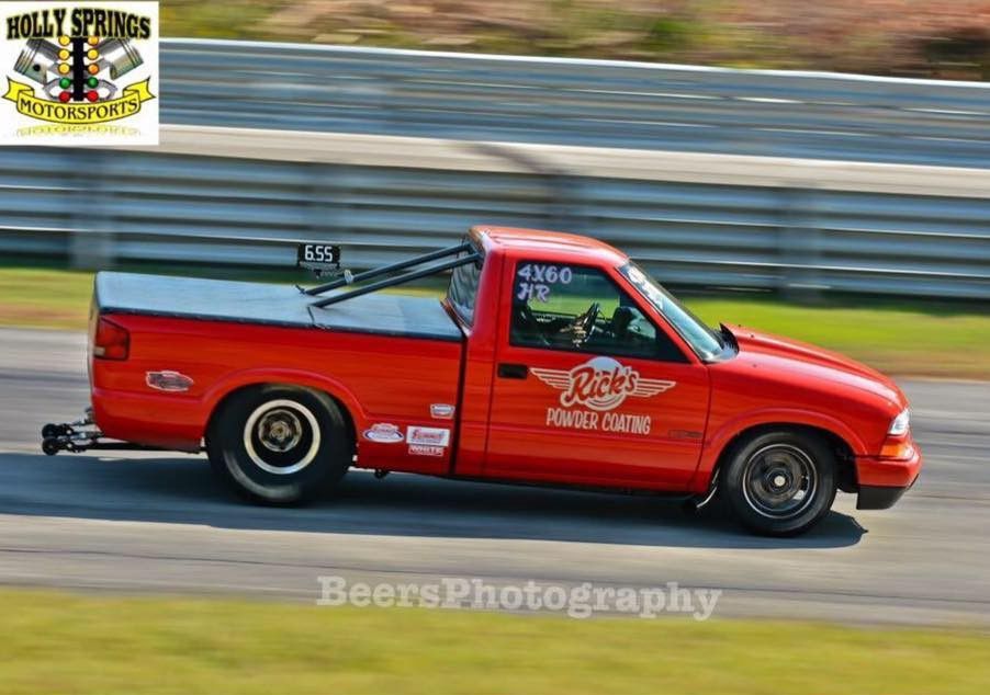 Red drag racing pickup truck speeding on a track with blurred background and sponsor decals