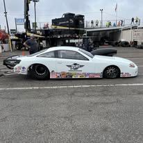 White race car with sponsor decals parked at an outdoor track, side view