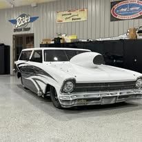 Classic white and black custom car with hood scoop displayed in a garage showroom