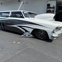 Custom white-and-black classic car with low stance and chrome details parked outside a garage