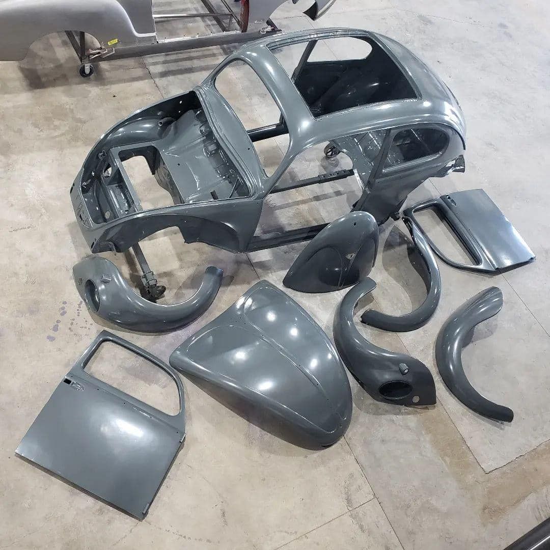 Scattered gray and black car body panels and trim pieces laid out on a workshop floor