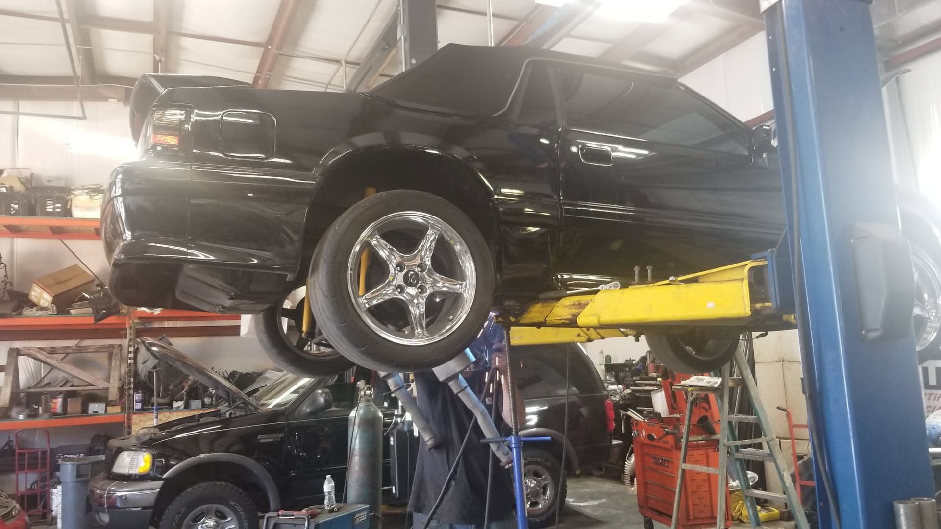 Black car lifted on a yellow hydraulic hoist inside an auto repair shop