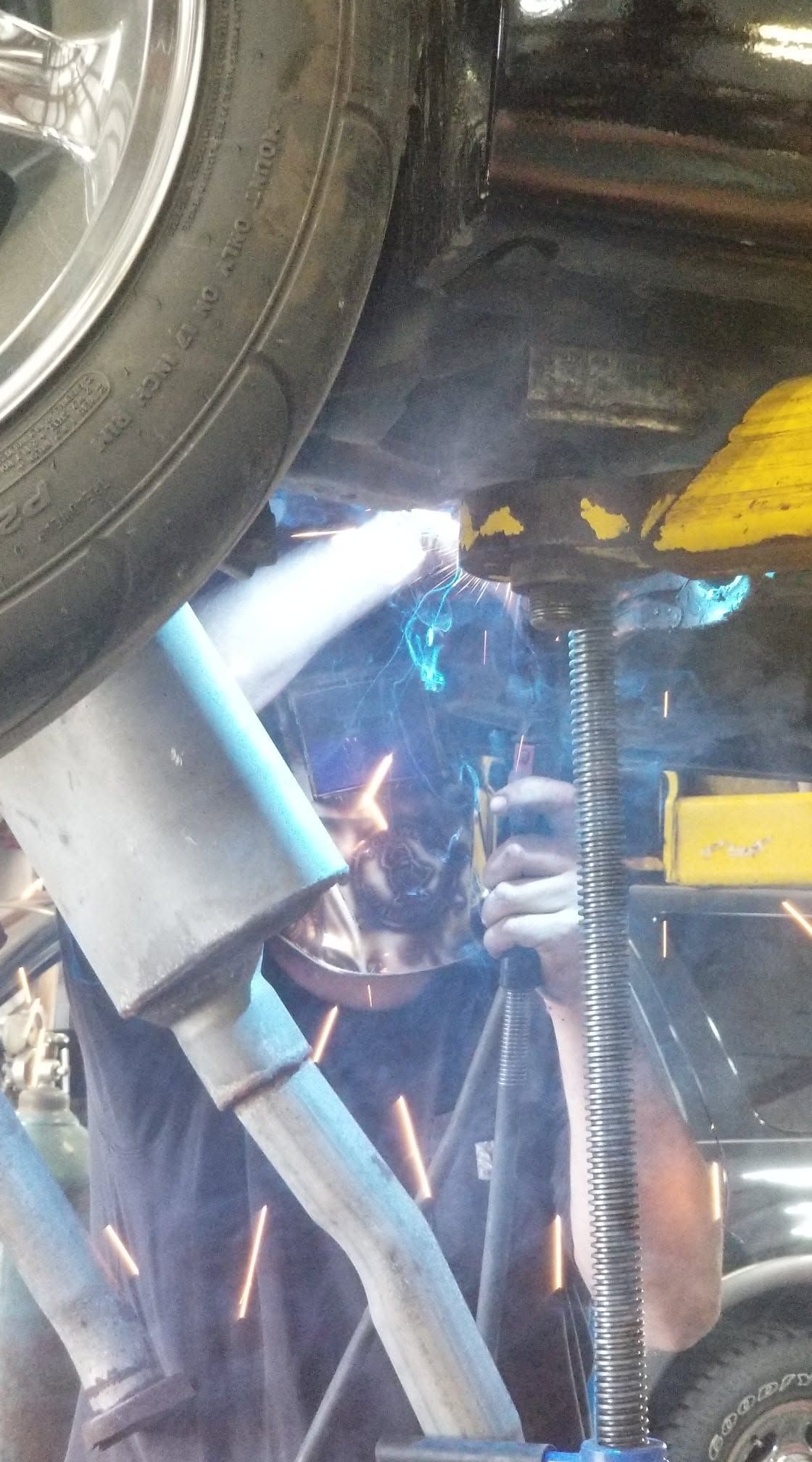 Welding sparks under a vehicle near a tire and blue jack stands in a garage