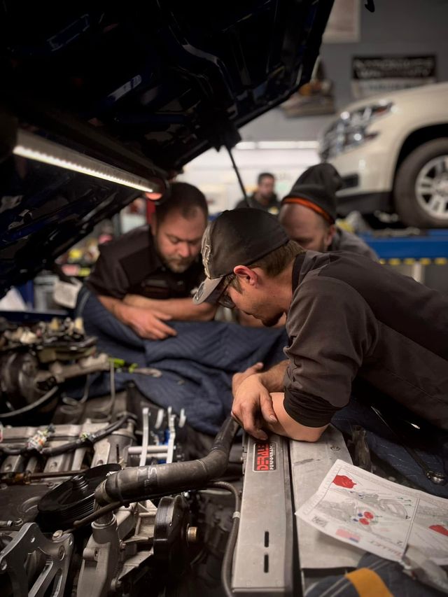 Mechanic team working under a car hood, inspecting the engine in a garage