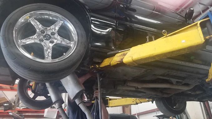 Black car on a yellow lift in an auto repair shop, viewed from below.