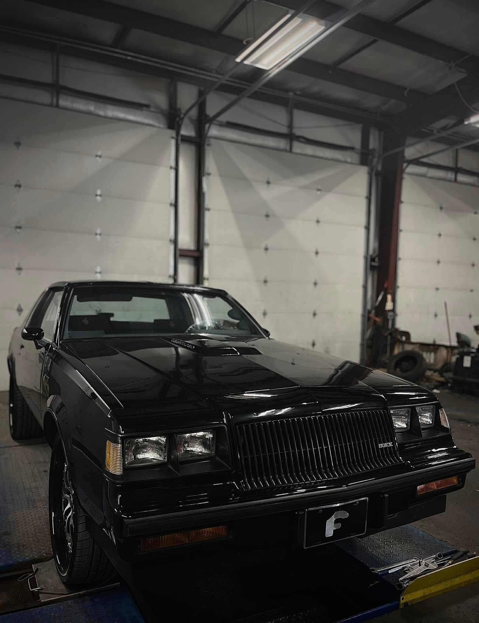 Black classic car in a garage, front view on a lift platform under bright industrial lights