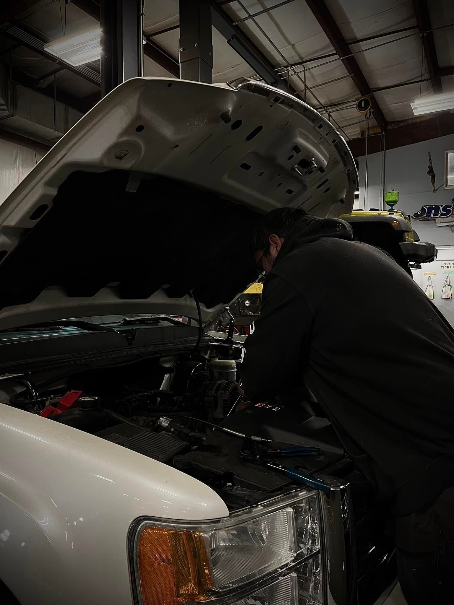 Person working under the hood of a white car in a garage