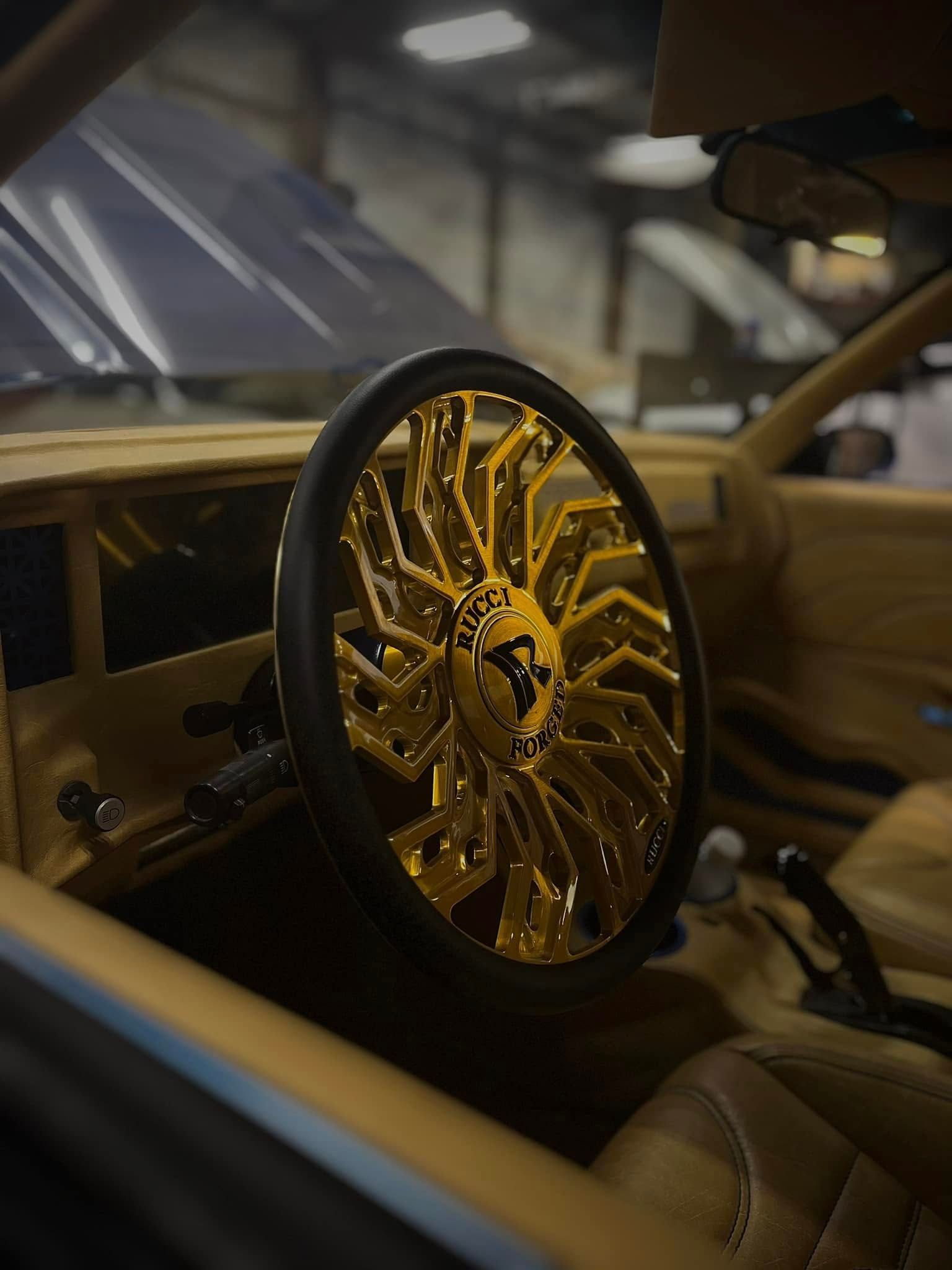 Gold custom wheel mounted inside a tan luxury car interior under dim lighting
