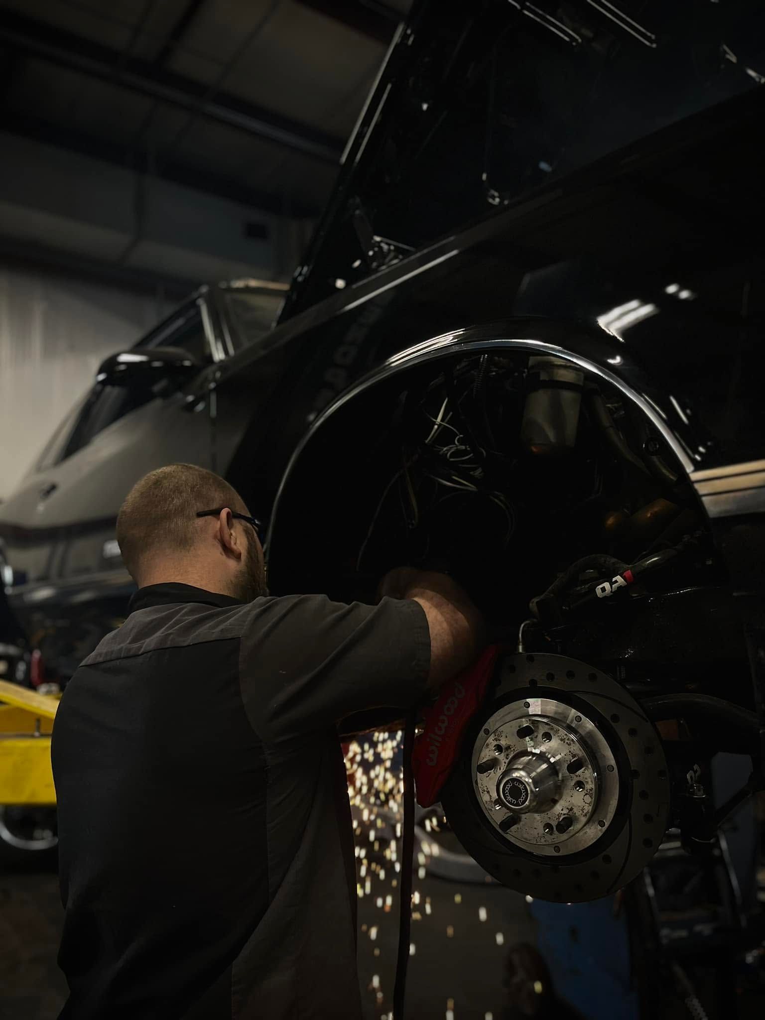 Mechanic grinding the wheel well of a black car in a workshop, sparks flying
