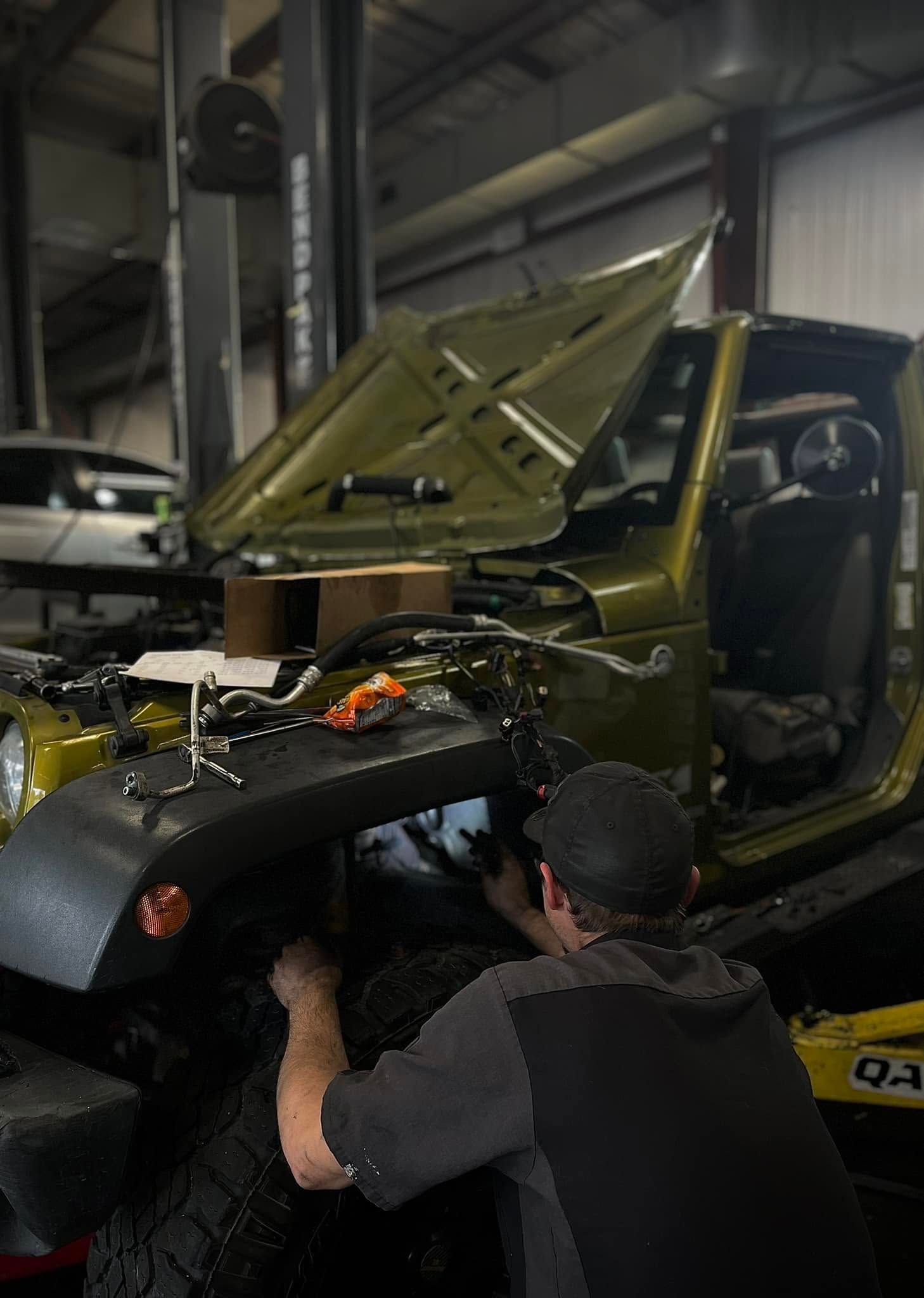 Mechanic working on an olive-green pickup truck with hood open inside a workshop