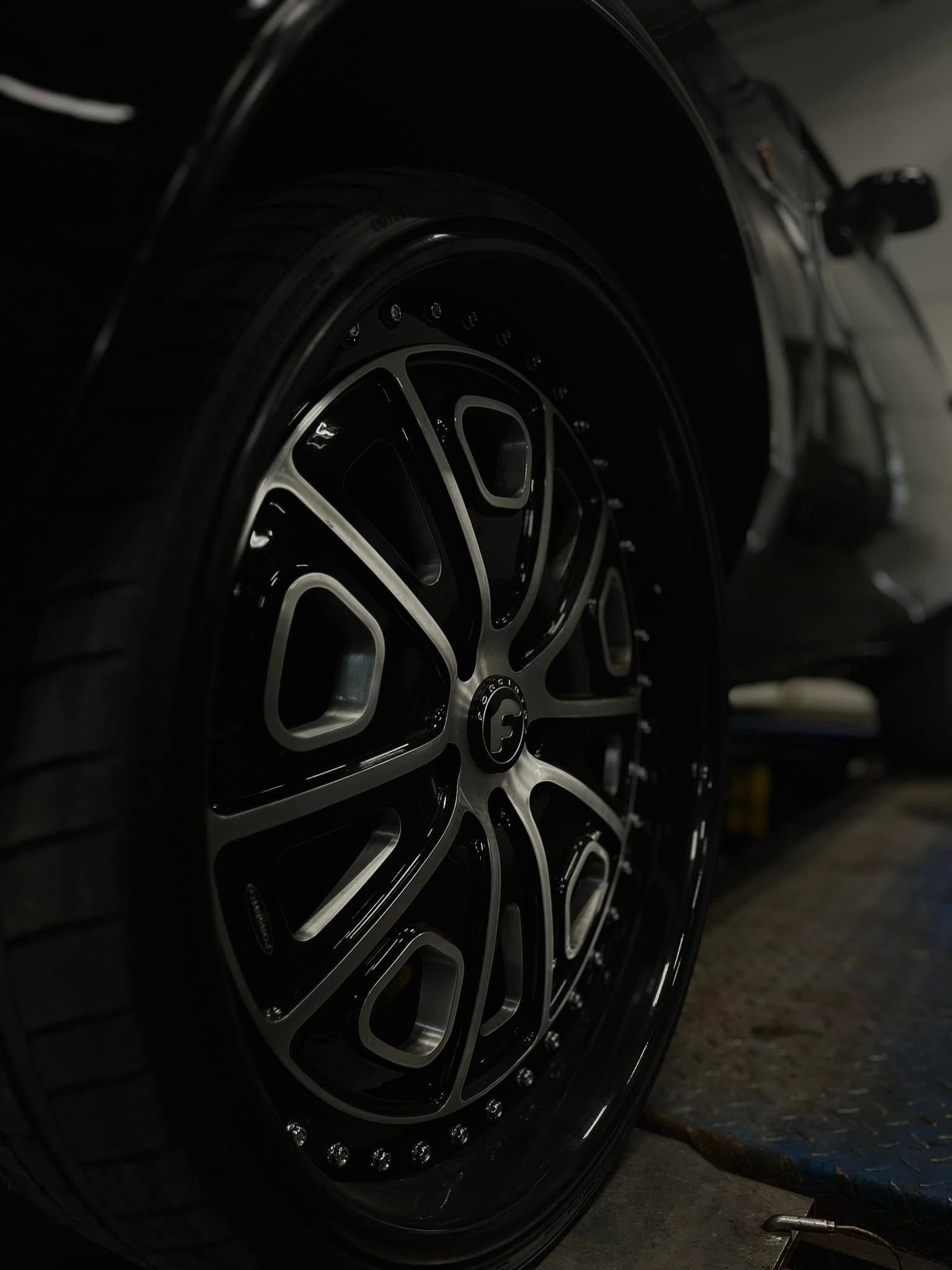 Close-up of a black car wheel with glossy custom rim in a dimly lit setting