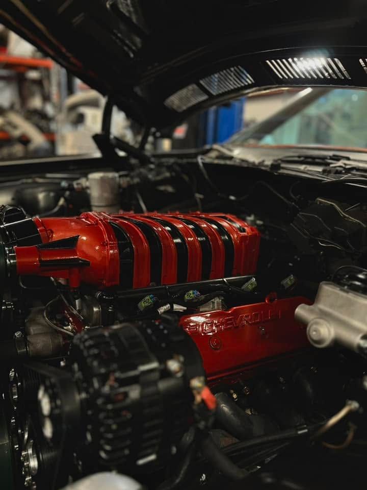 Close-up of a car engine bay with a red supercharger and black components under the hood