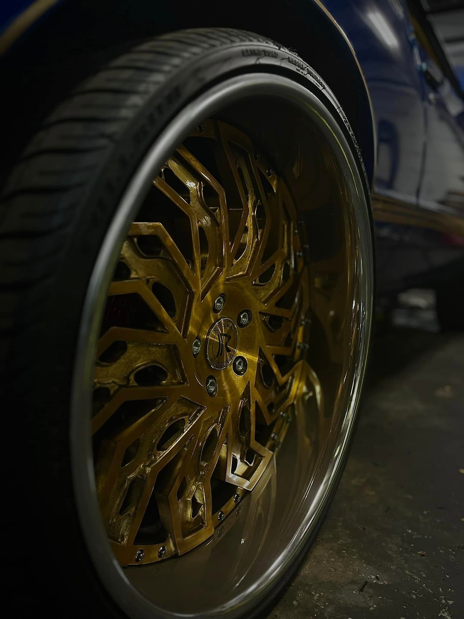 Gold custom car wheel with intricate spokes, parked on dark pavement at night