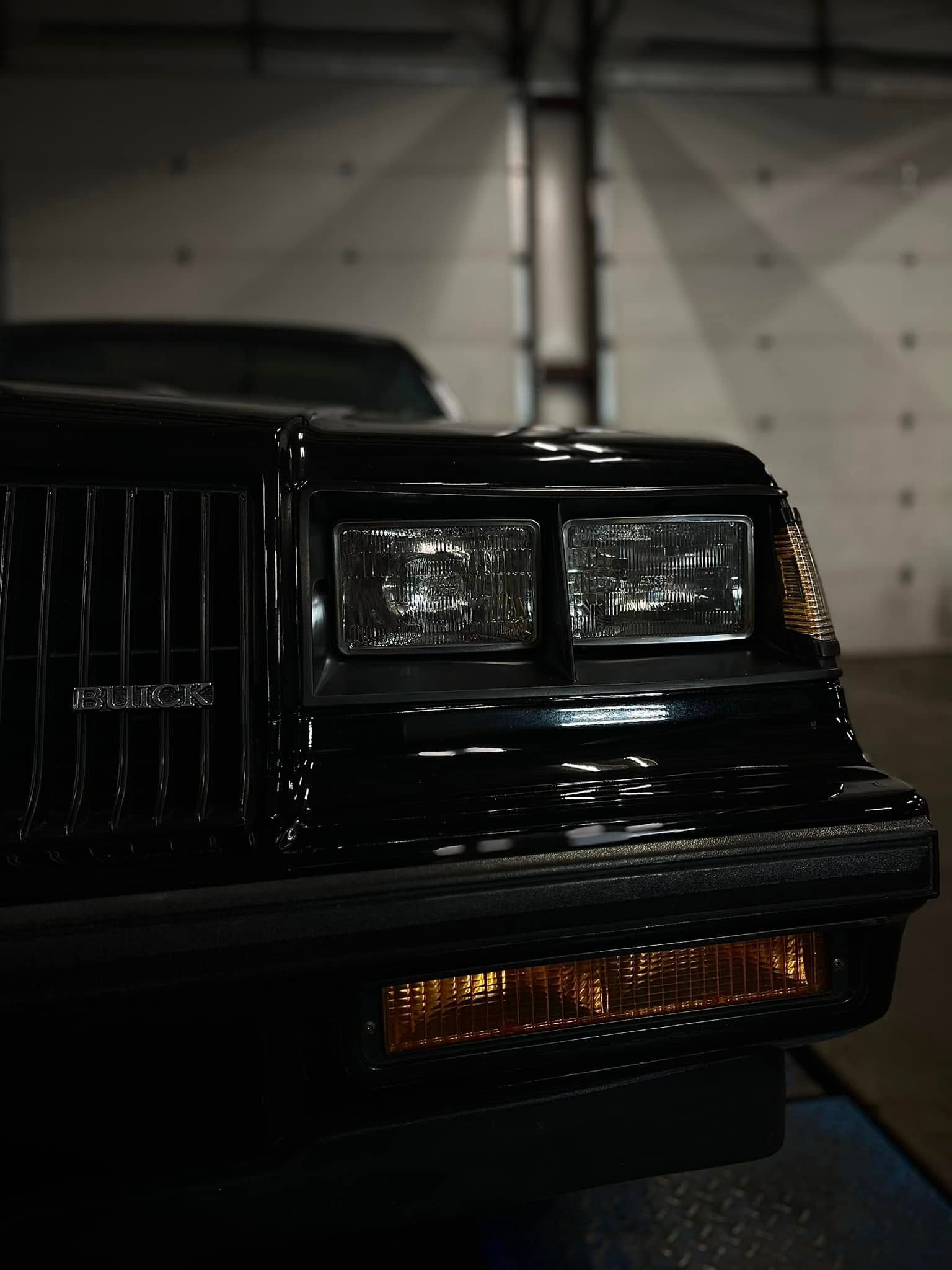 Front of a black classic car with rectangular headlights in a garage