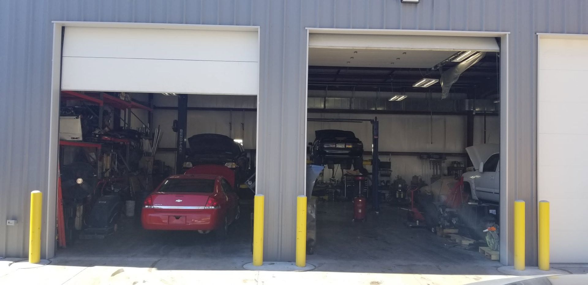 Two open garage bays with vehicles and equipment inside, including a red car on the left.