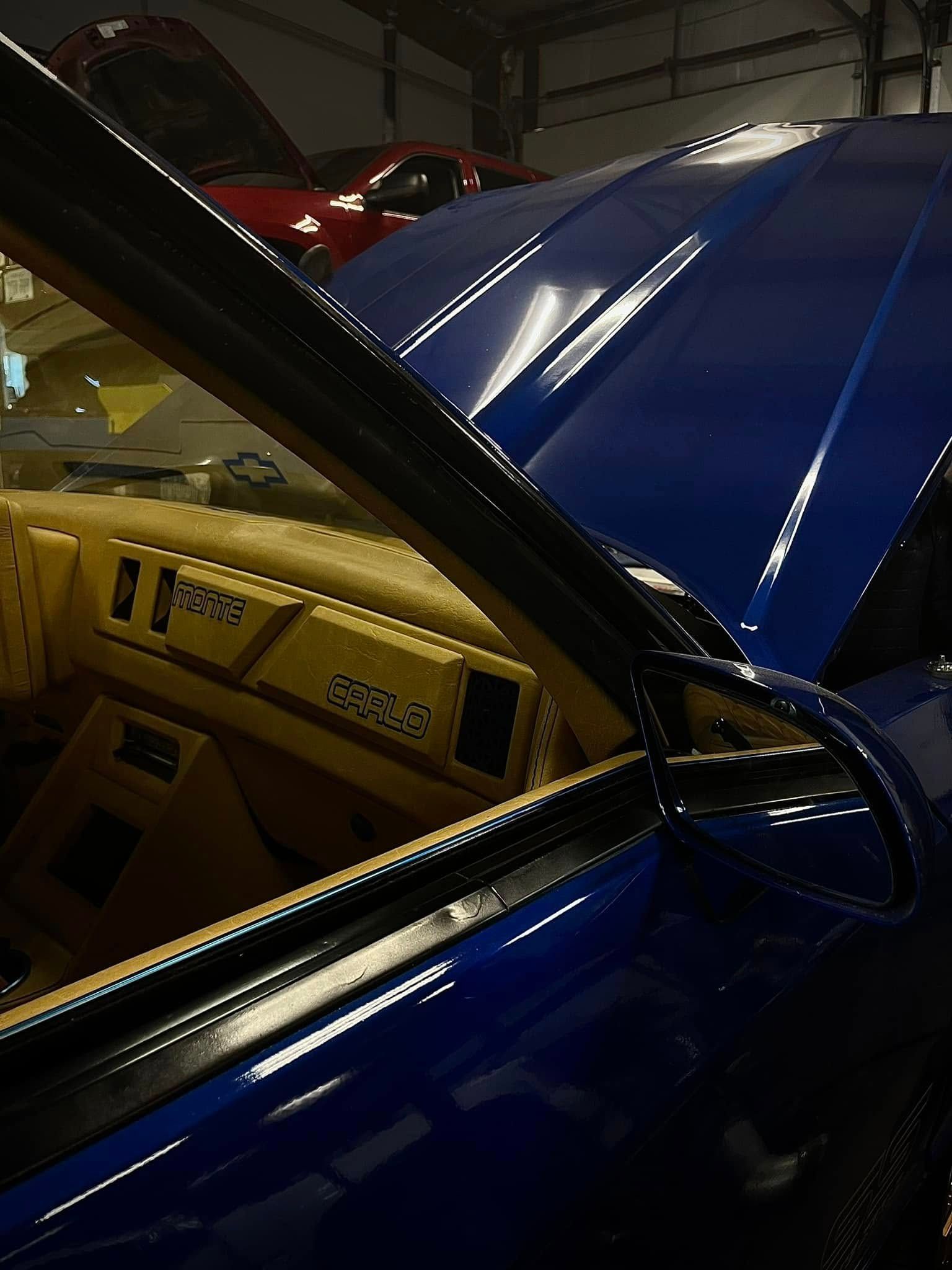 Close-up of a blue car with its hood open, showing a tan interior and engine bay at an auto show