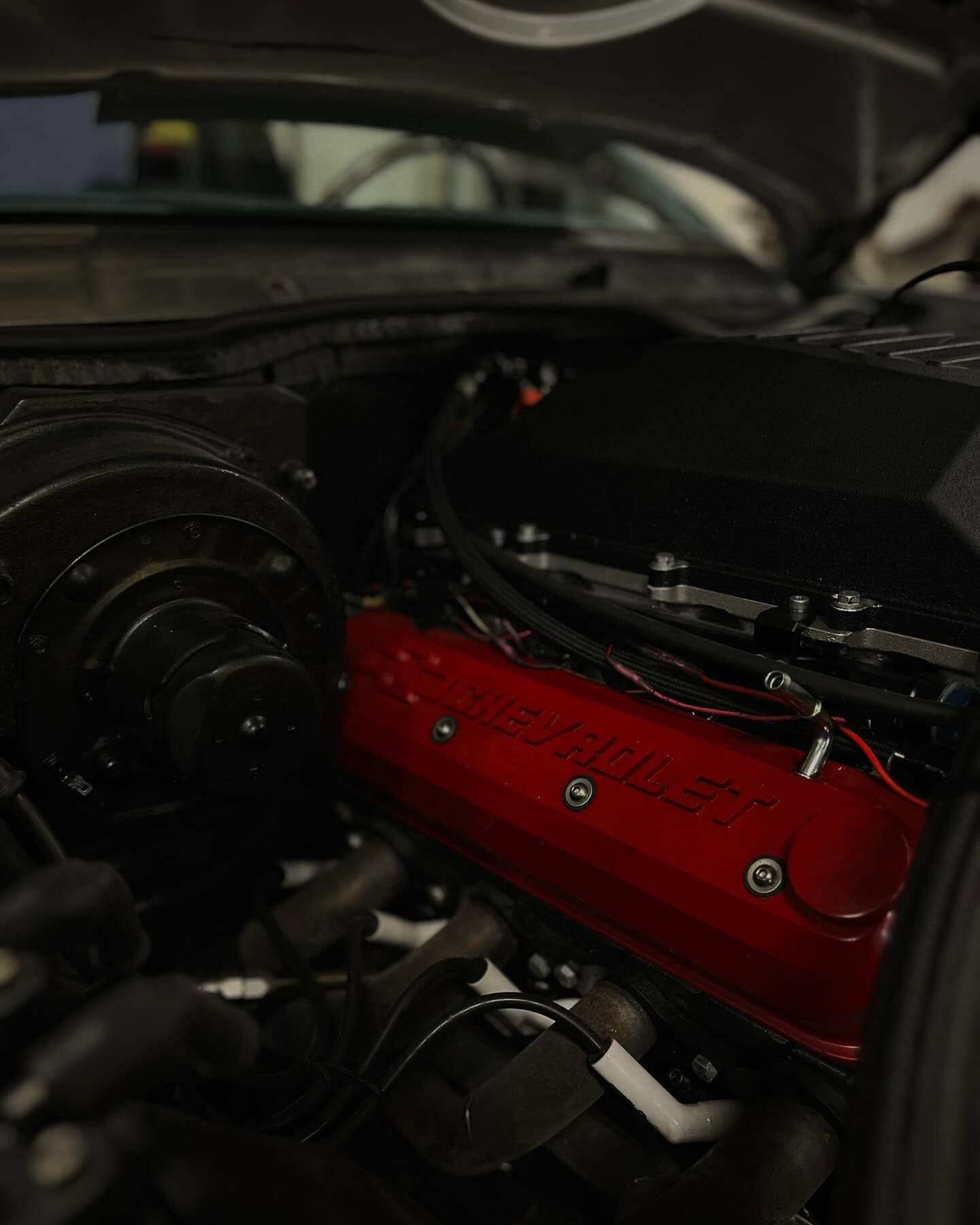Close-up of a car engine bay with a red valve cover and black components under the hood