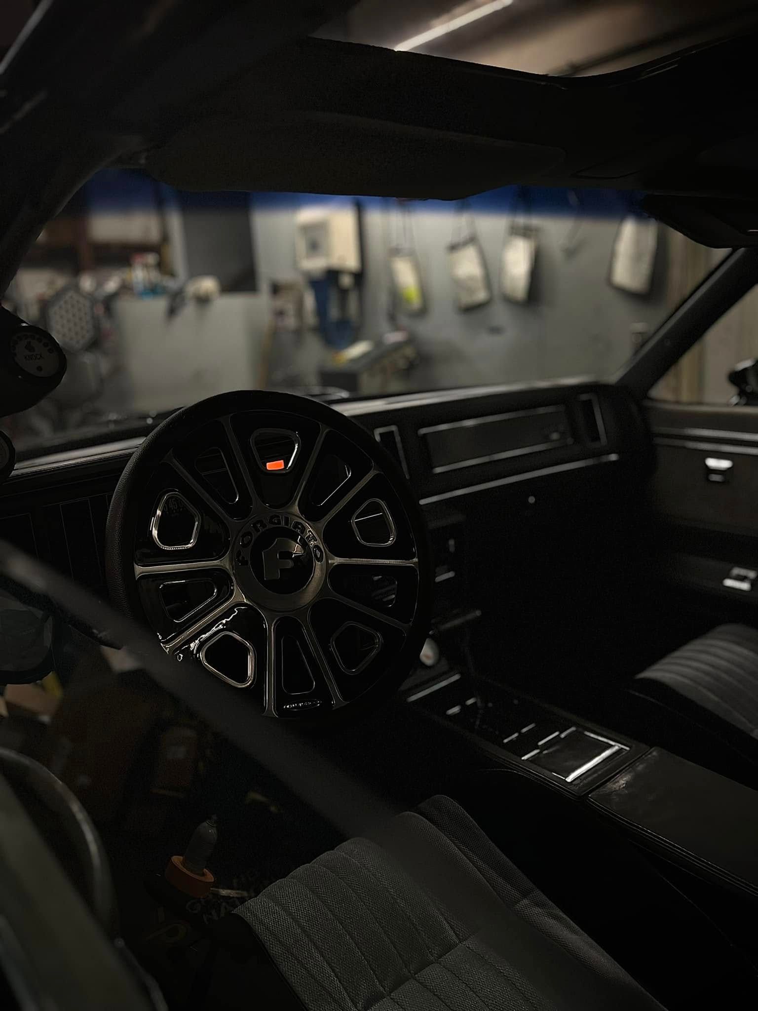 Dark car interior with a black steering wheel and dashboard, seen from the driver’s seat