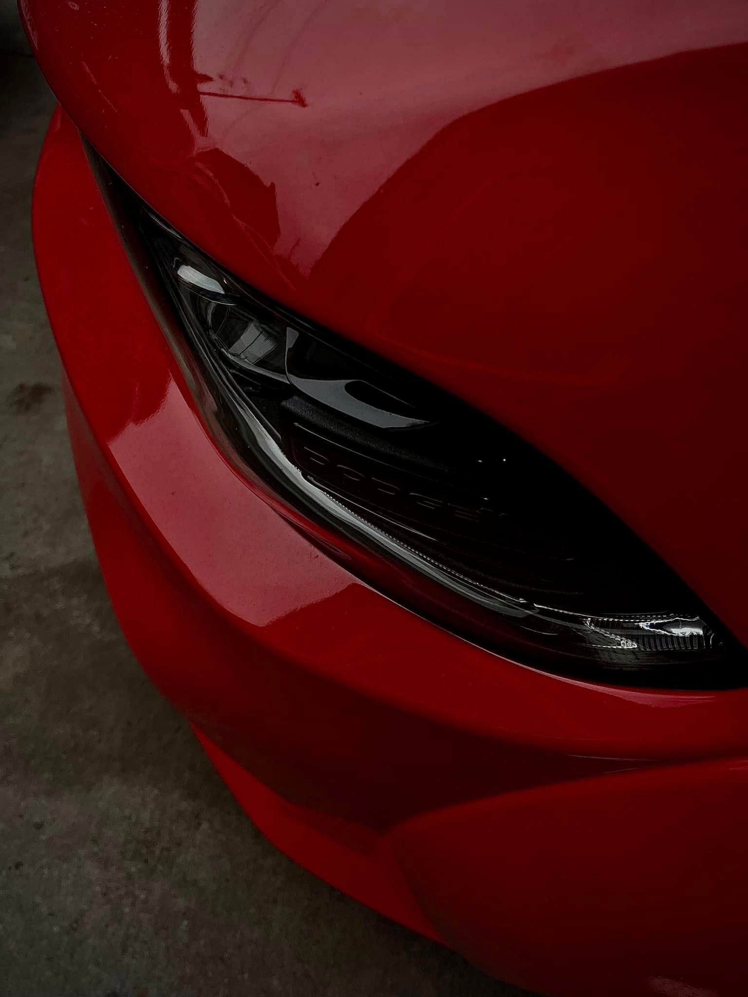 Close-up of a glossy red sports car front headlight and bumper detail