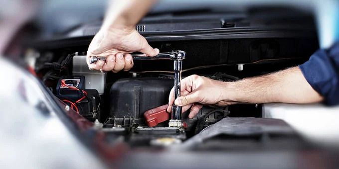 Mechanic using a ratchet wrench to repair a car battery in the engine bay