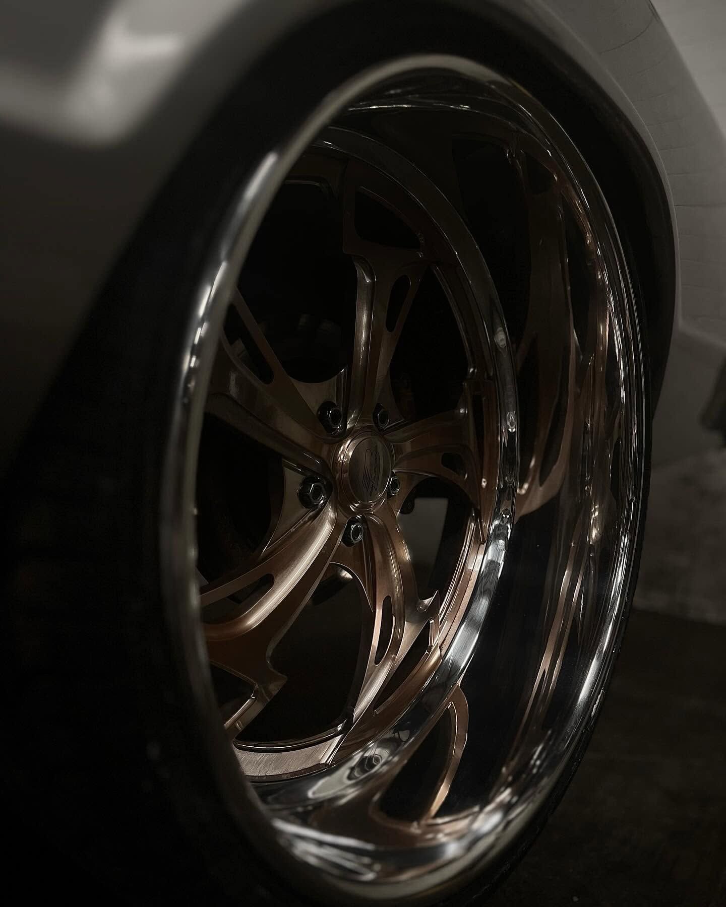 Close-up of a shiny chrome car wheel rim in a dimly lit garage.