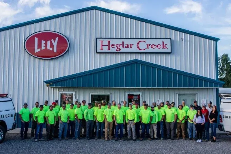 A group of people wearing matching lime green shirts stand in front of a building labeled Lely and Heglar Creek.