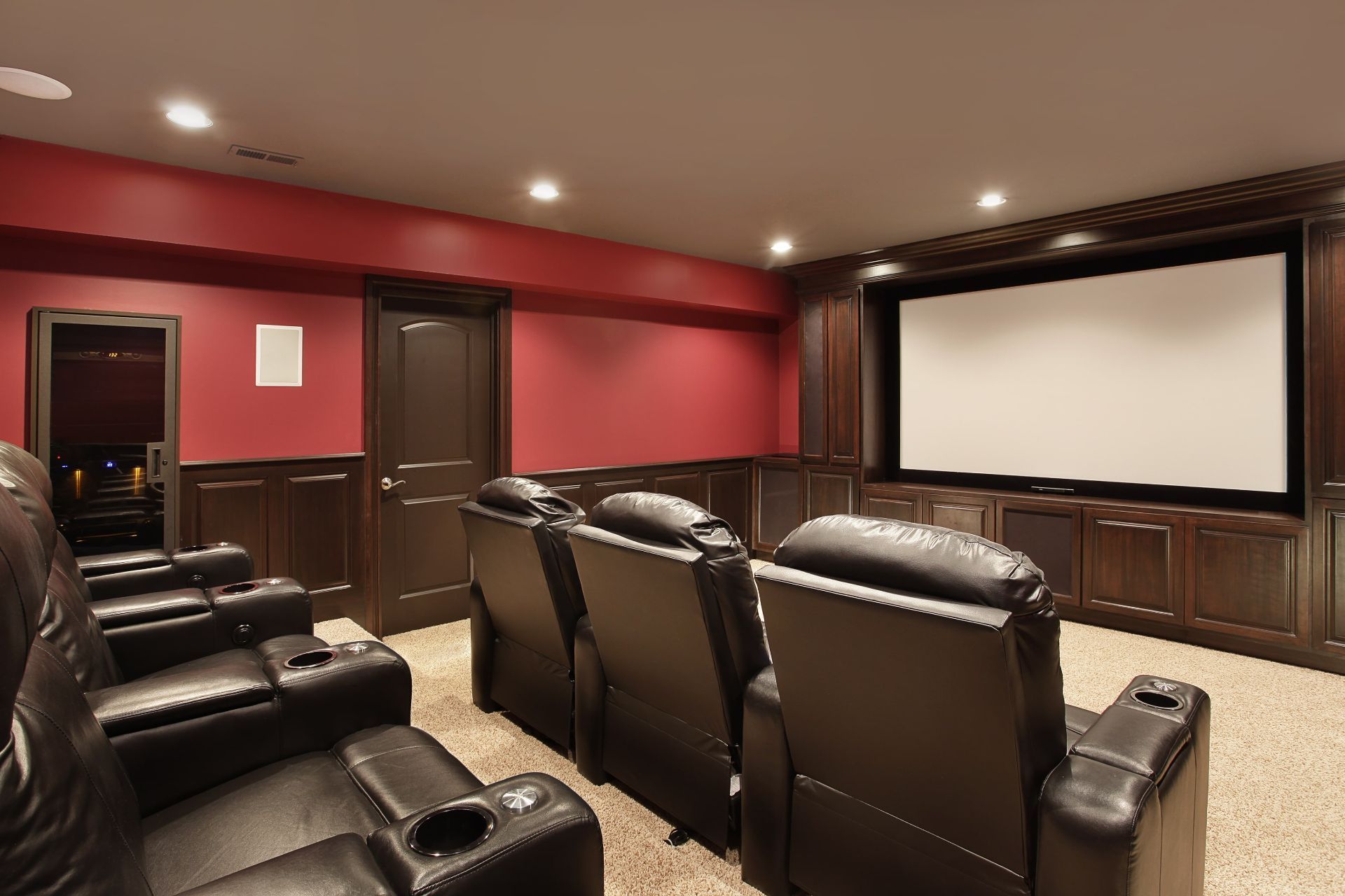 Home theater room with black leather recliners, red walls, and a large projection screen