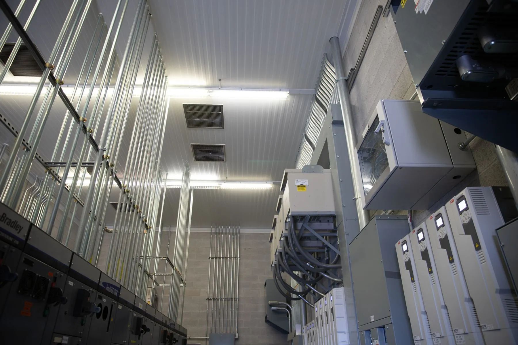 Low-angle view of an industrial control room with electrical cabinets, metal racking, and overhead lighting.