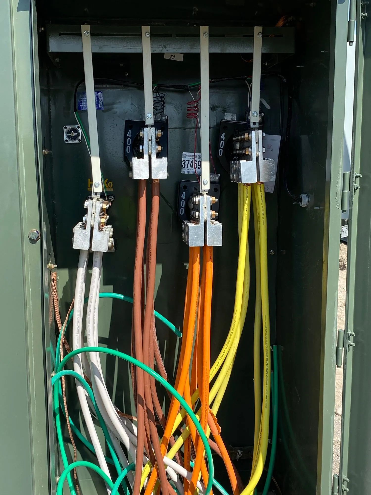 Open electrical panel with multicolored wires and breakers inside a green metal cabinet