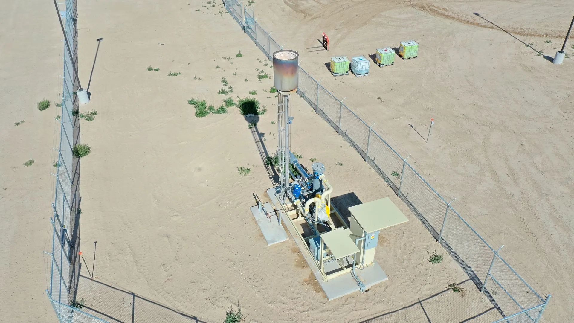 Desert campsite with a small utility structure, tents, and people beside utility poles and a dirt road