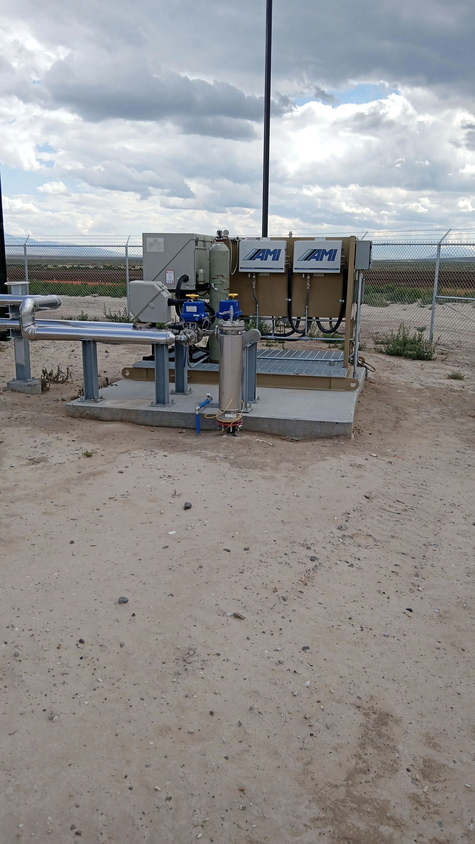 Outdoor industrial equipment with pipes and a control box on a sandy site under cloudy sky