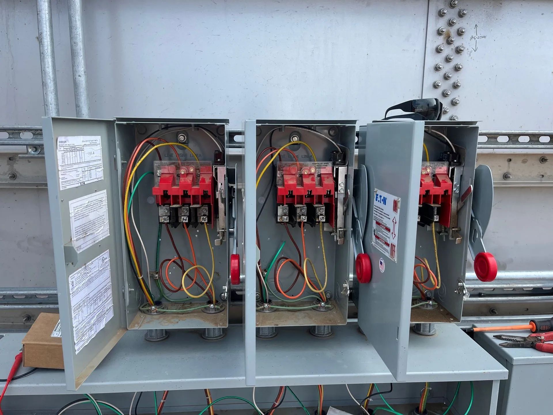 Open electrical control panels with wiring and red switches mounted on a metal frame.