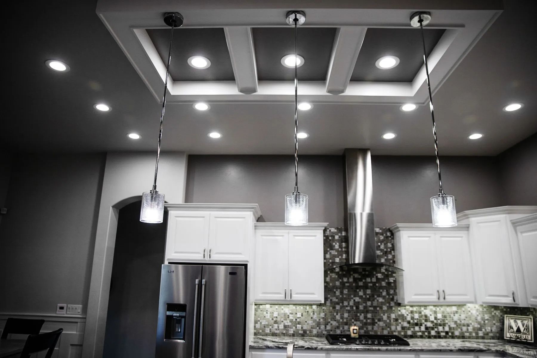 A modern kitchen featuring white cabinets, stainless steel appliances, a tiled backsplash, and three hanging glass lights.