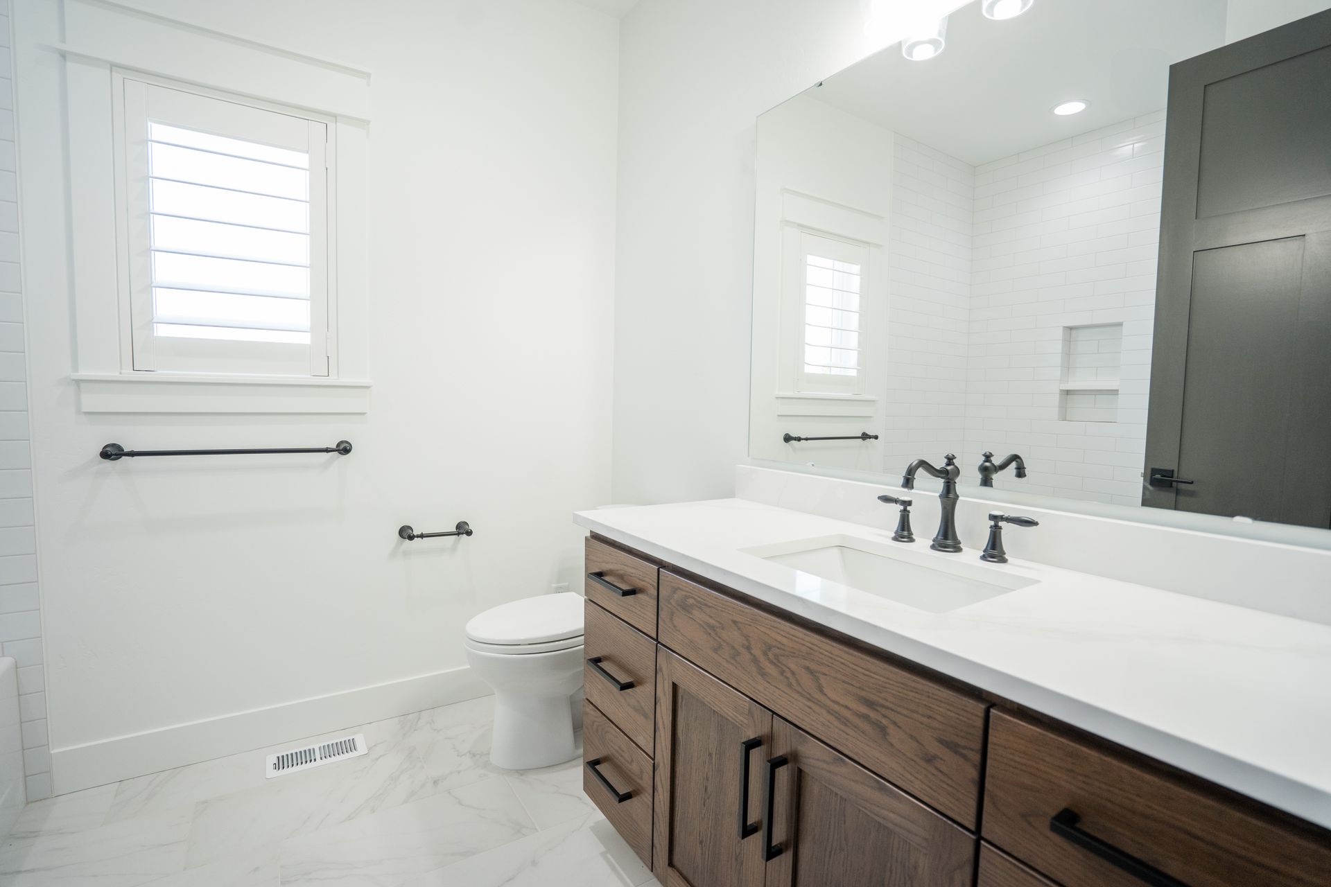 Bright modern bathroom with double vanity, large mirror, toilet, and white tile walls