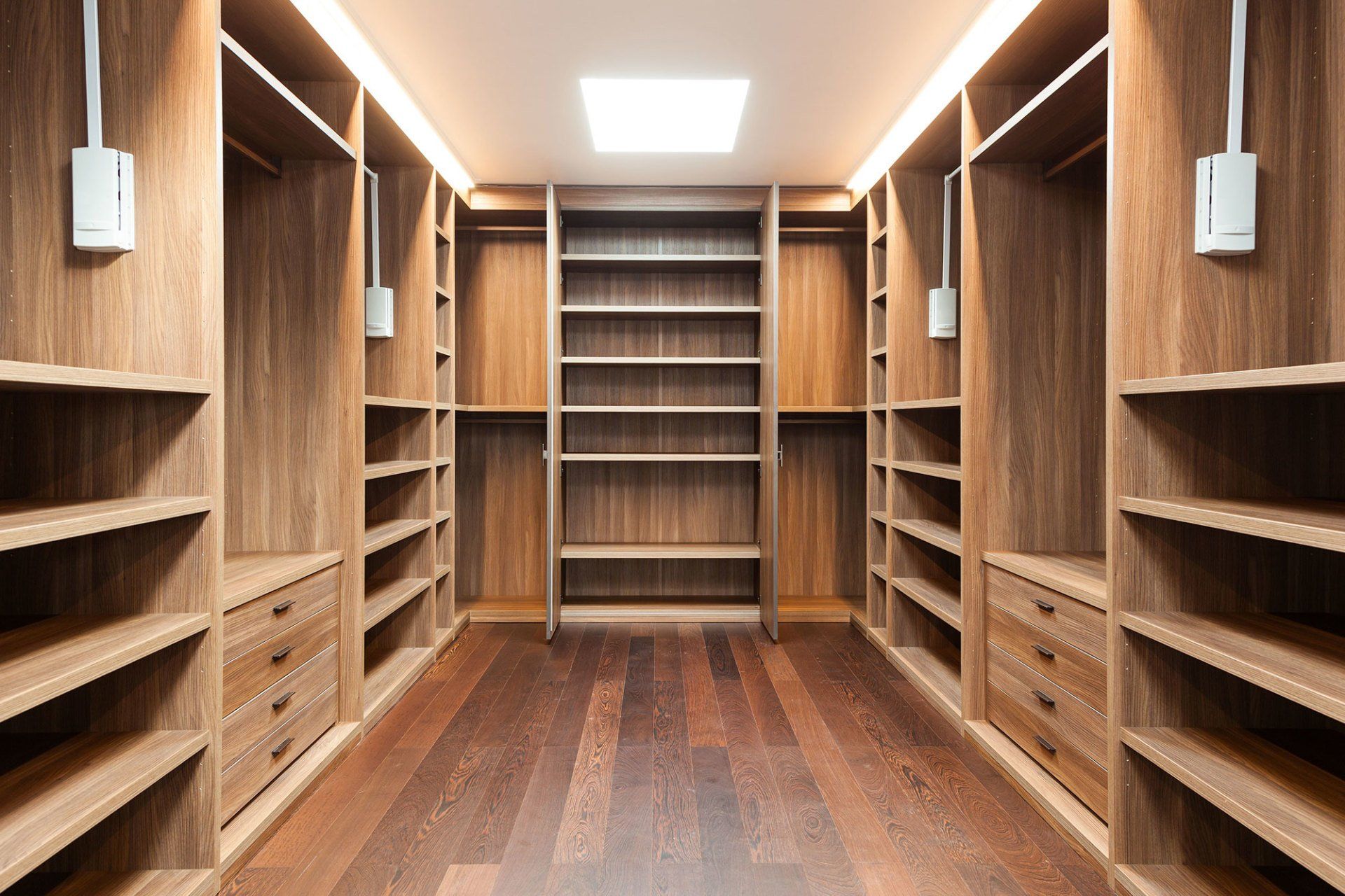 Wood-paneled walk-in closet with built-in shelves and drawers, centered under bright ceiling lights