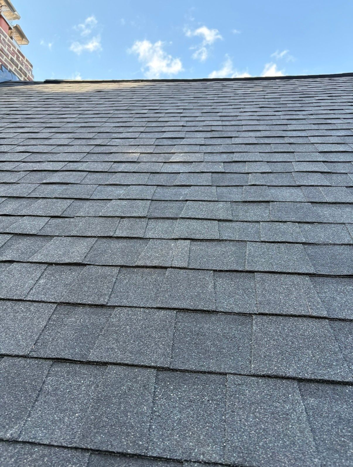 Gray shingled roof under a blue sky with scattered clouds