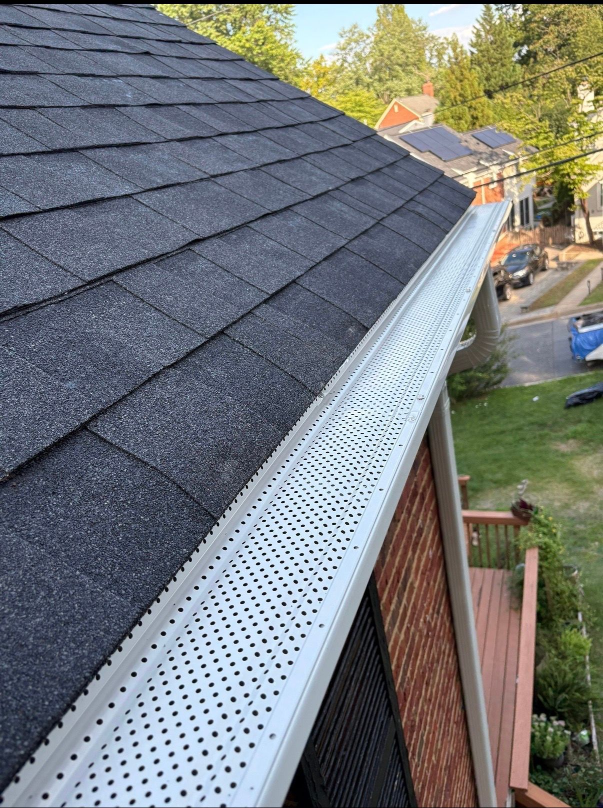 Perforated metal gutter guard along a roof edge beside dark gray shingles and a yard below