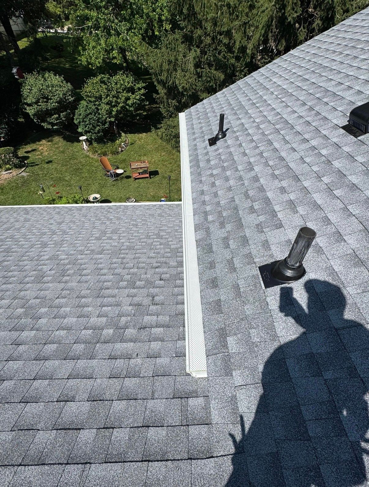 Roof shingles with two vent pipes and a person’s shadow overlooking a grassy yard below