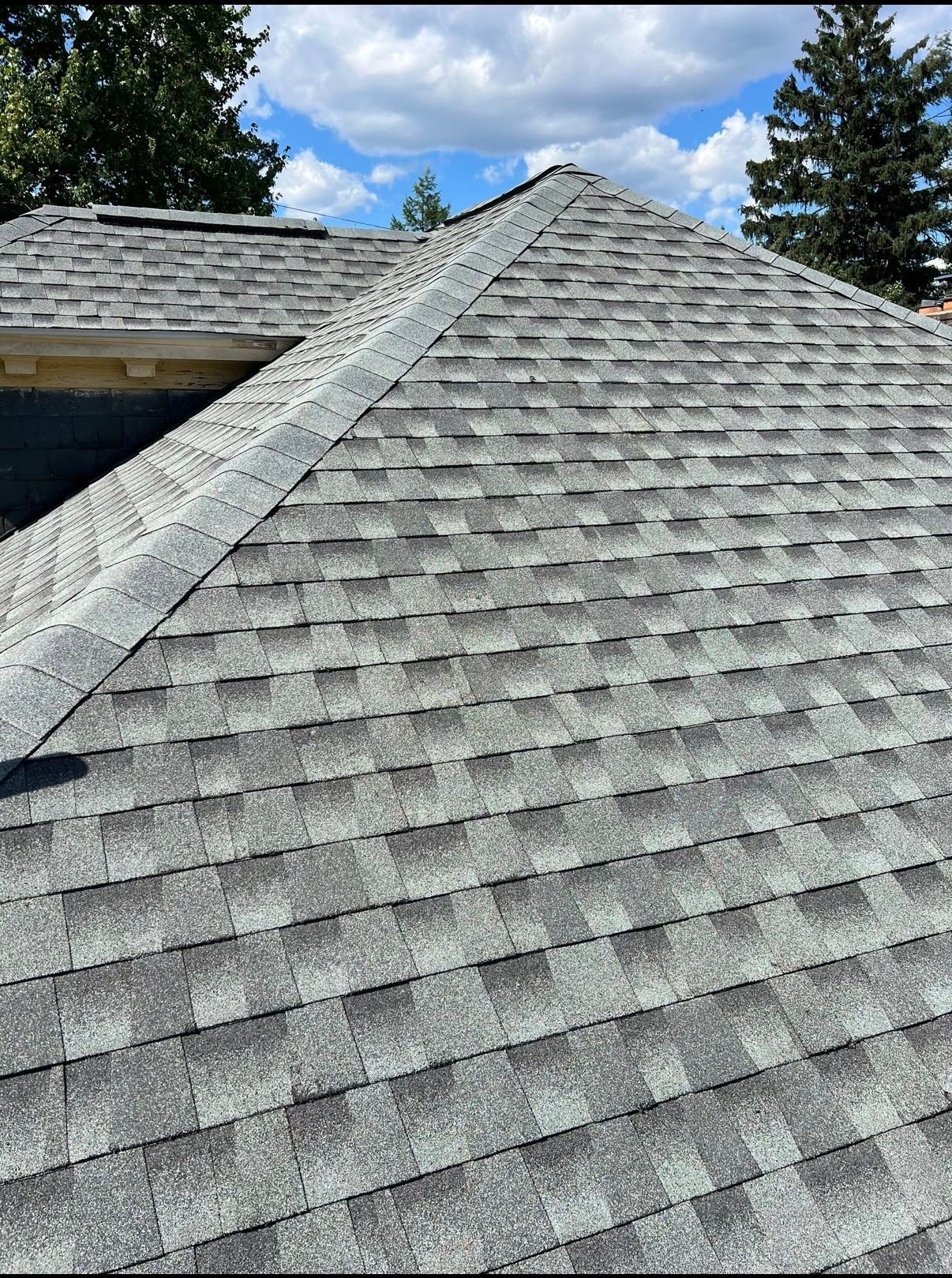 Gray shingle roof with skylight under a partly cloudy blue sky