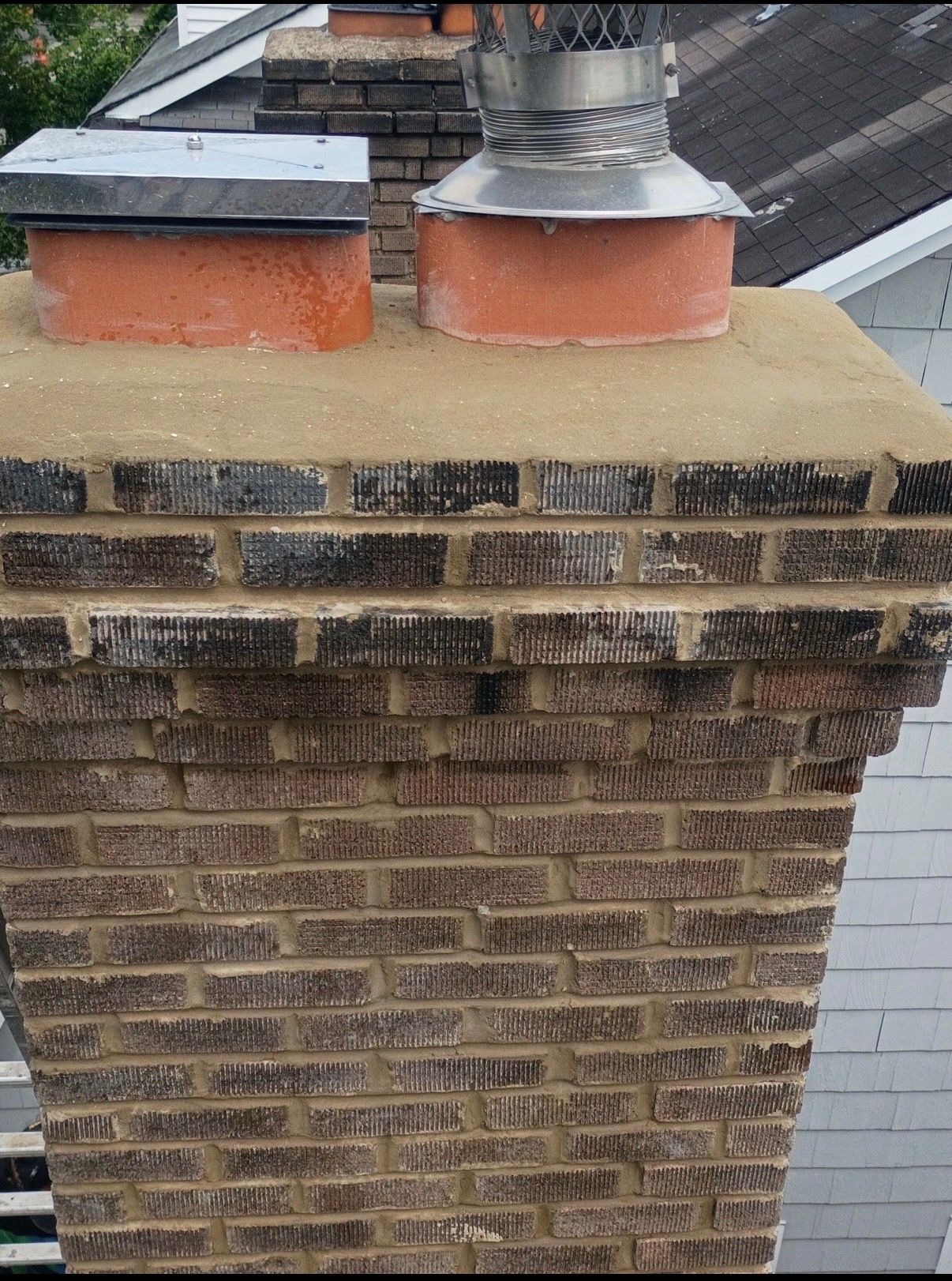 Brick chimney with two flues and weathered black smoke staining near the top on a rooftop