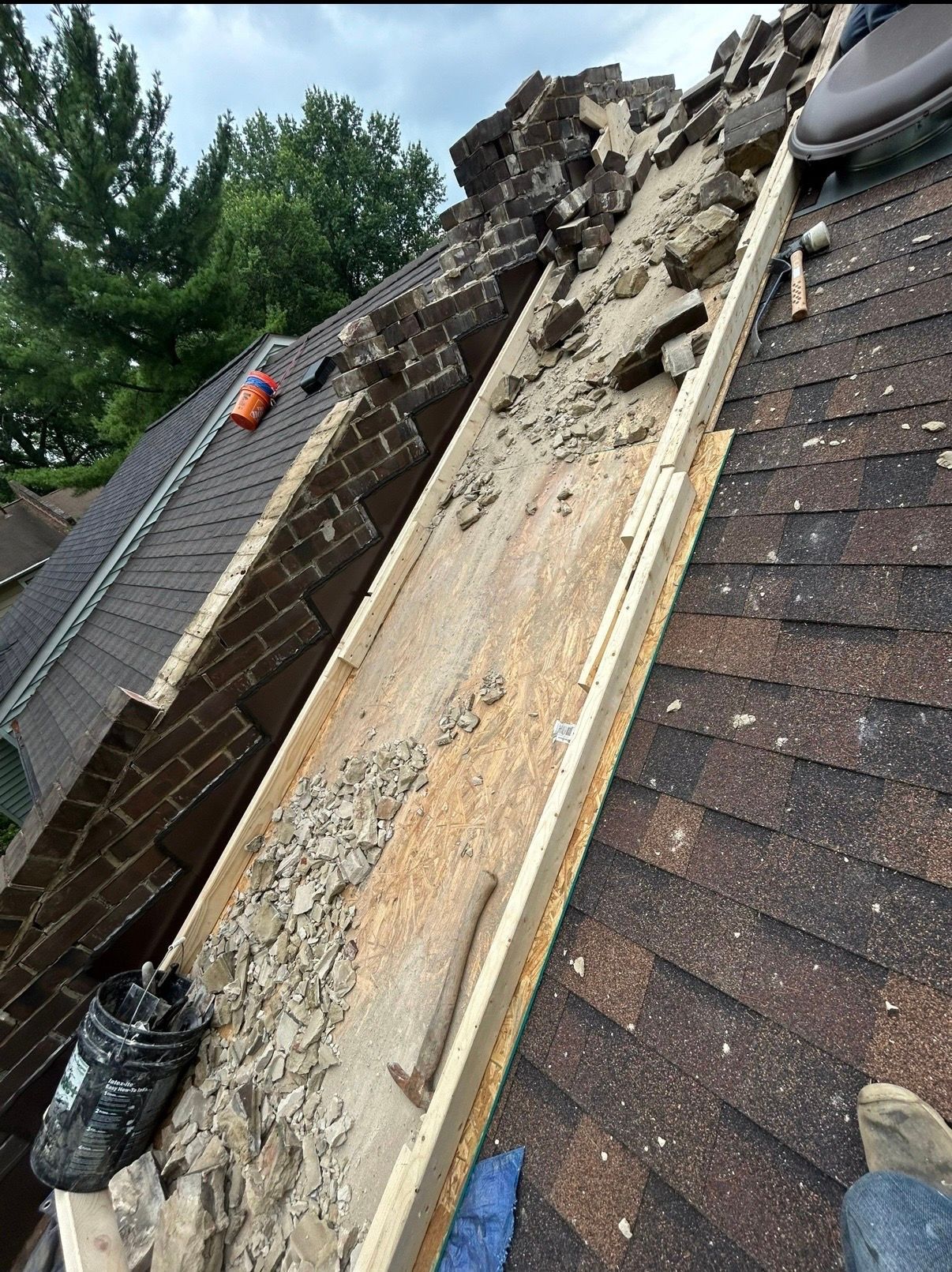 Collapsed roof repair with debris, exposed wood, and damaged brick chimney alongside shingles